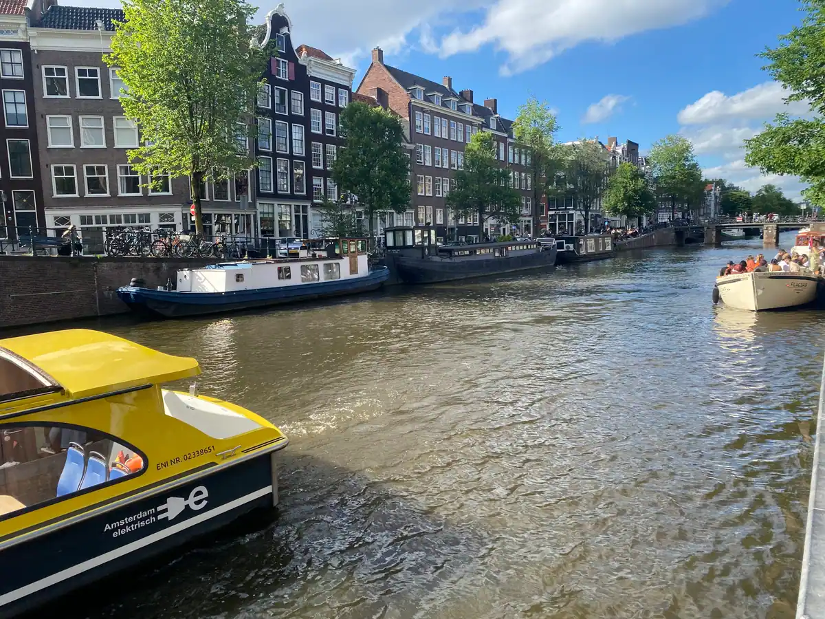 A canal with houseboats and a moored launch, with a row of narrow houses along the far bank.
