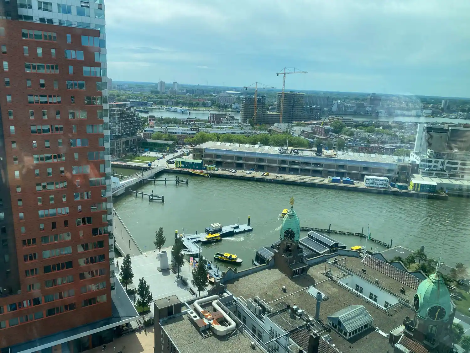 A view over a waterfront with quays and cranes, an orange building rising at the left, taken through glass.