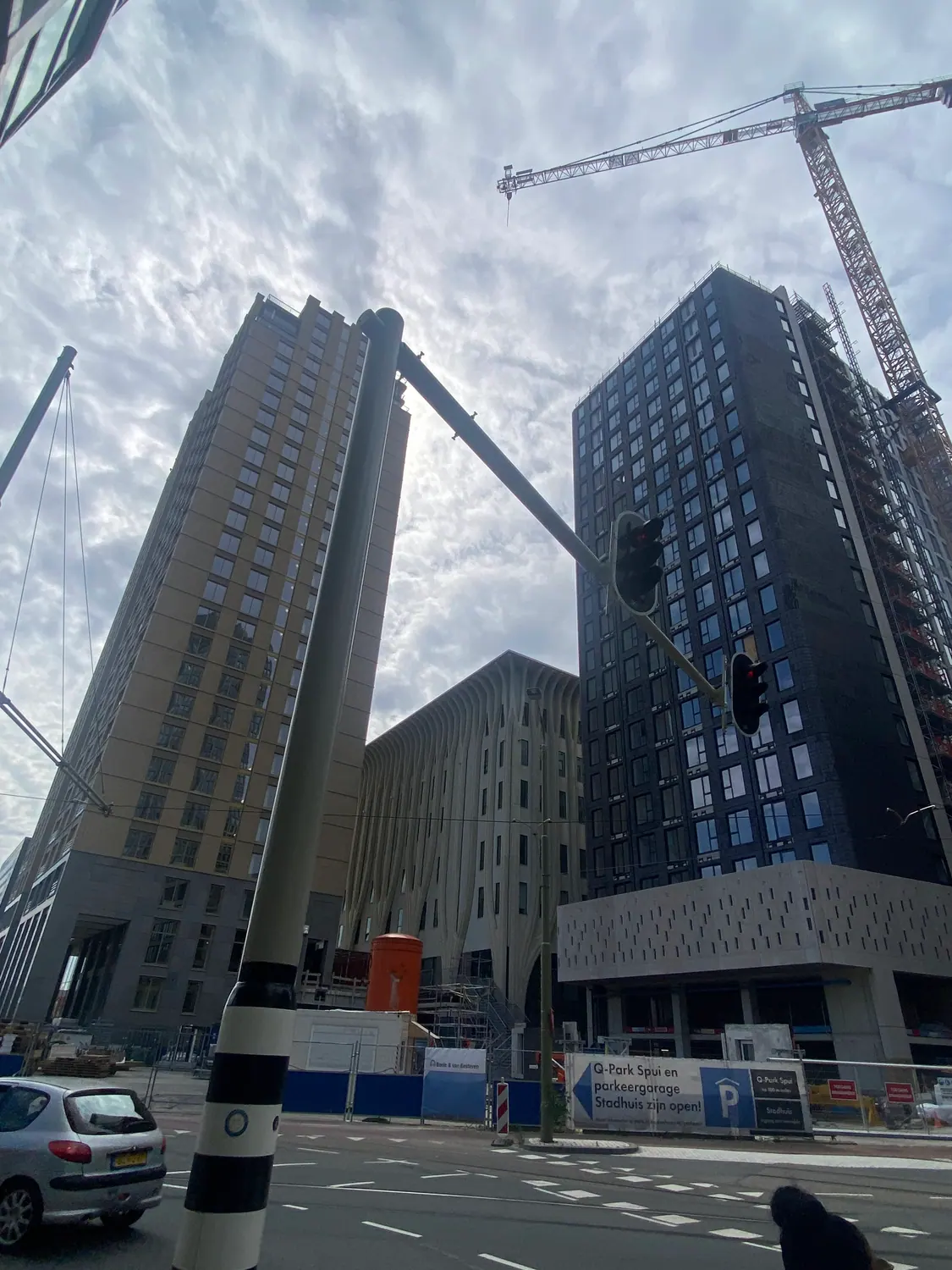 A street corner where tower blocks meet, a crane above them, with traffic lights and a car in front.