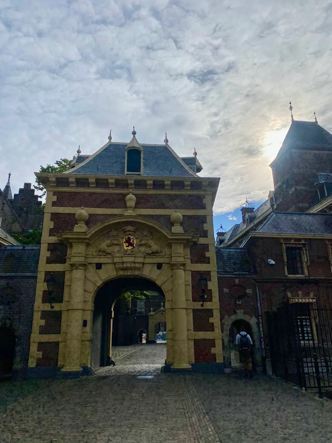 A brick gatehouse with an arched passage and a carved crest above it, one person walking through the arch.