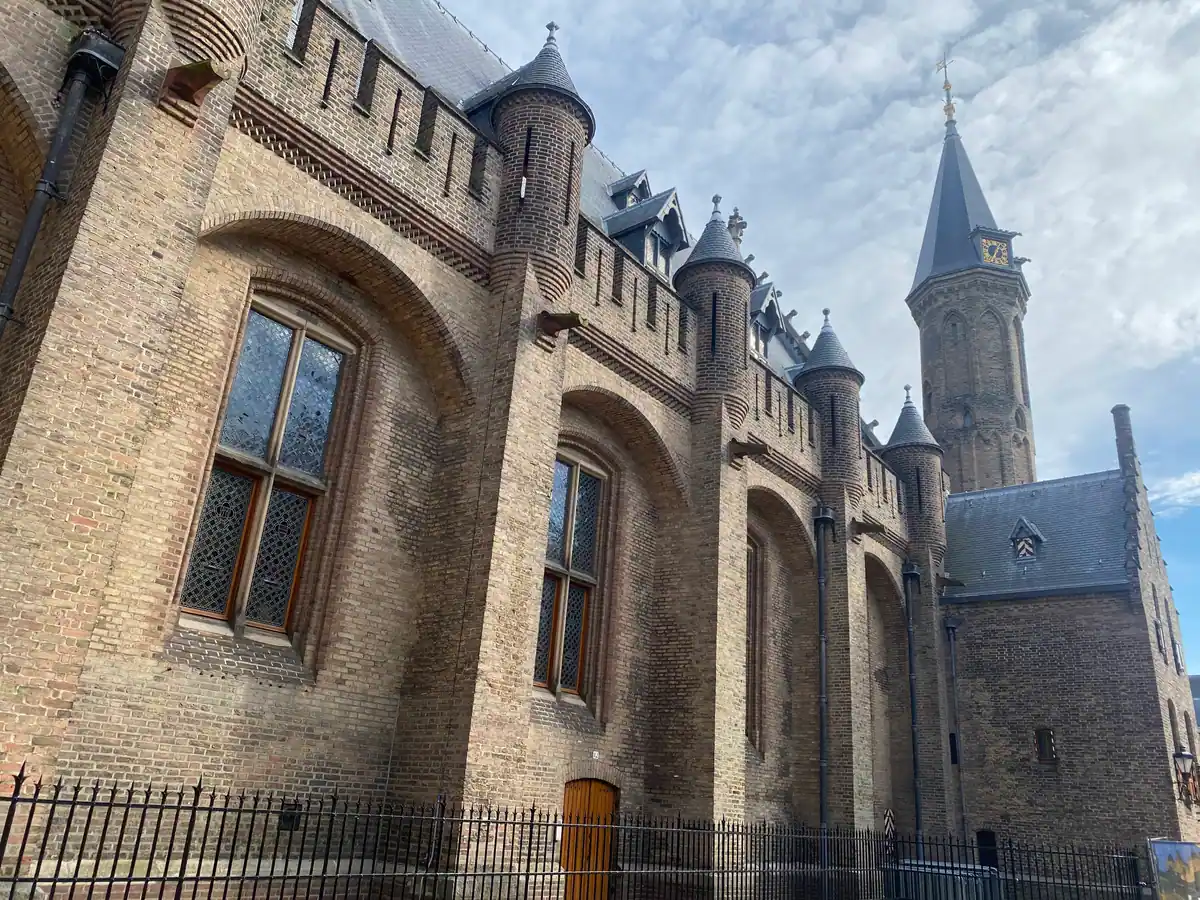 A brick hall with tall arched windows, a stair turret and a tower, with iron railings below.