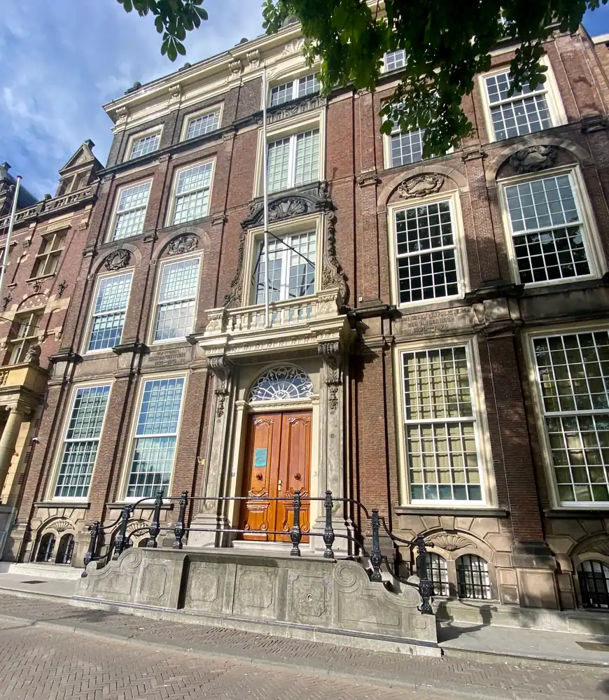 A tall ornate townhouse front of brick and stone with a carved doorway, iron steps and a railing.
