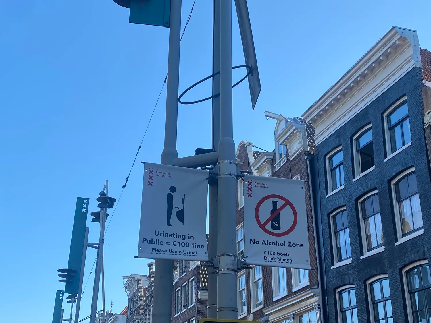 Two printed street notices fixed to a pole, with buildings behind them.
