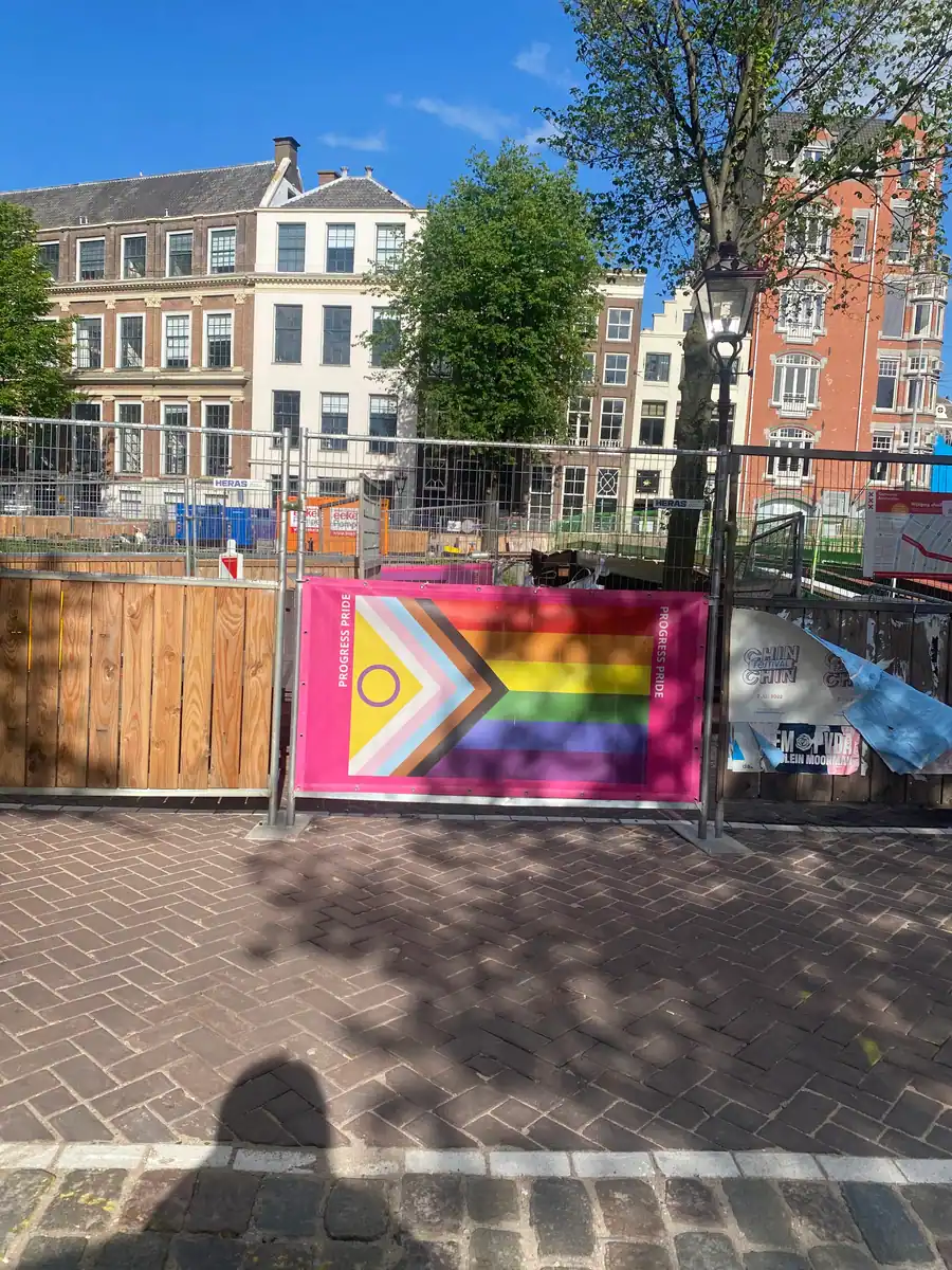 A street of brick houses behind a timber hoarding and scaffolding net, with a printed banner fixed to the hoarding.