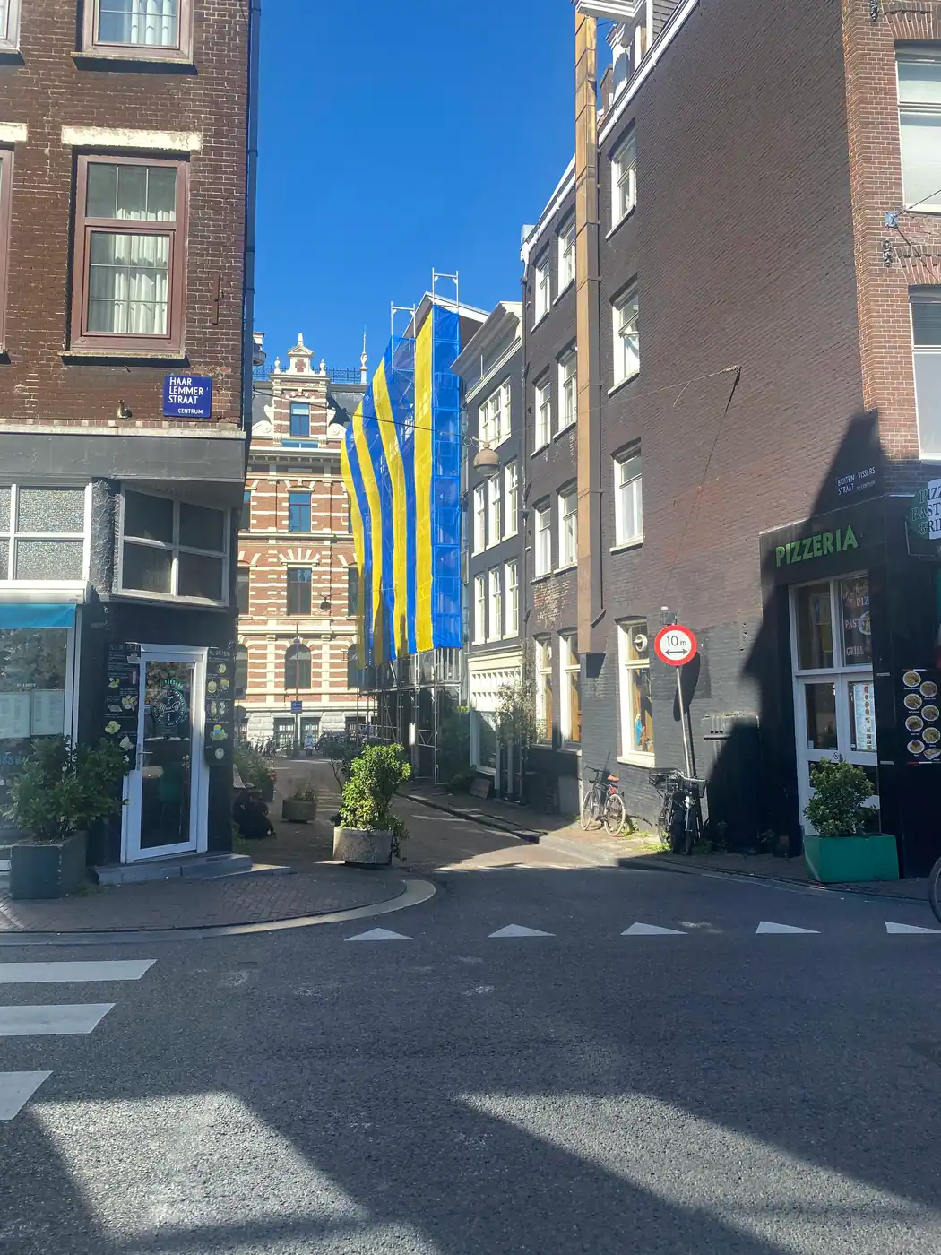 A street corner of brick houses with a blue enamel street sign, a small shop front and a painted banner hung across it.