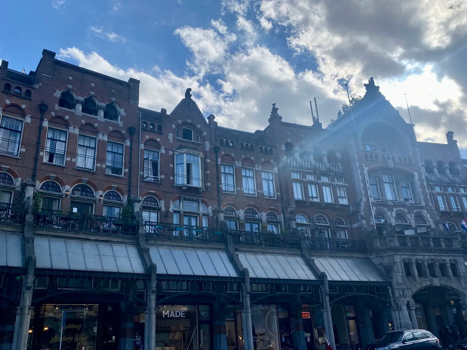 A row of brick buildings with shops and awnings at street level and cars parked along the front.