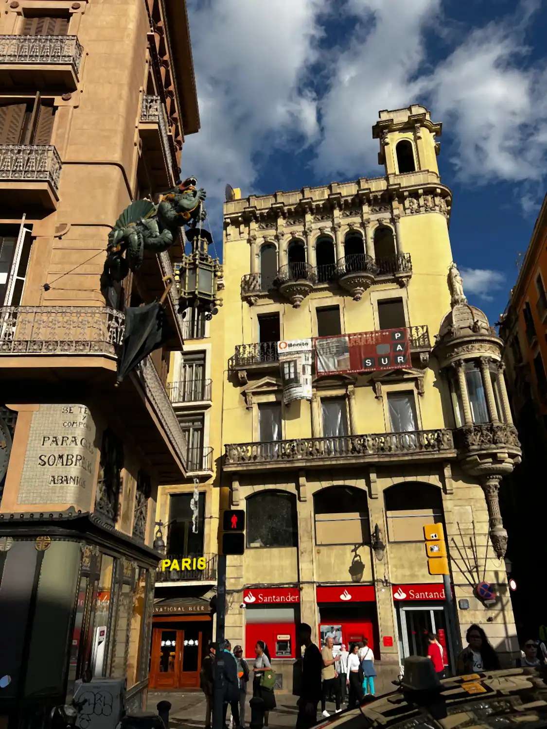 A yellow corner building with balconies and shopfronts, seen along a street.