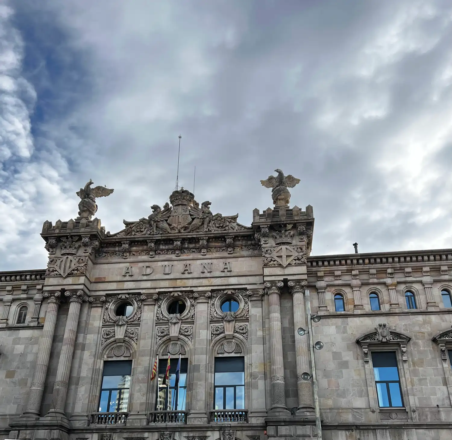 A stone civic building with a sculpted roofline and statues, seen from the street under grey cloud.