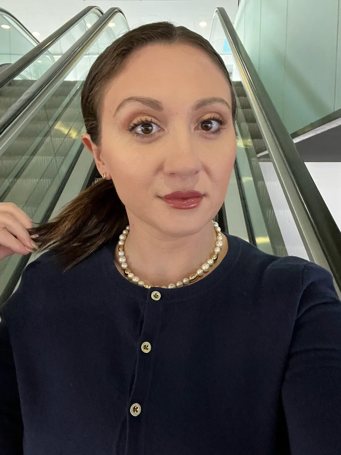 A woman in a dark top standing in a glass lift, looking at the camera.