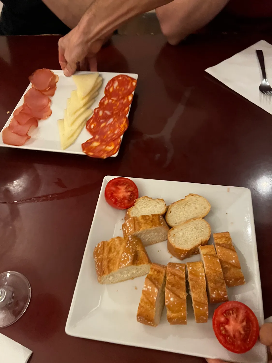 A plate of sliced cured meat and cheese on a table, bread with tomato on a second plate.