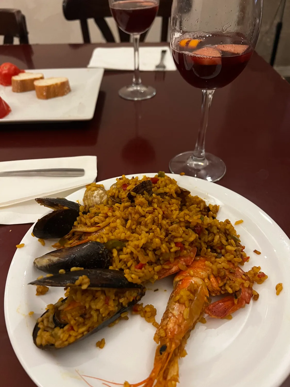 A plate of rice with a mussel and a prawn, two glasses of red wine behind it.