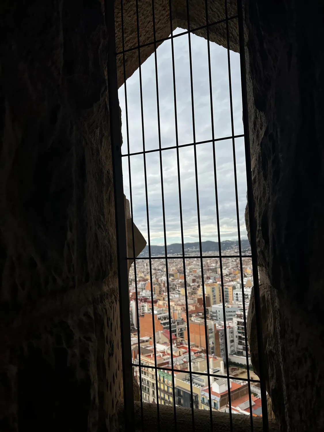 A city seen far below through a deep stone window opening, an iron grille in front of it.