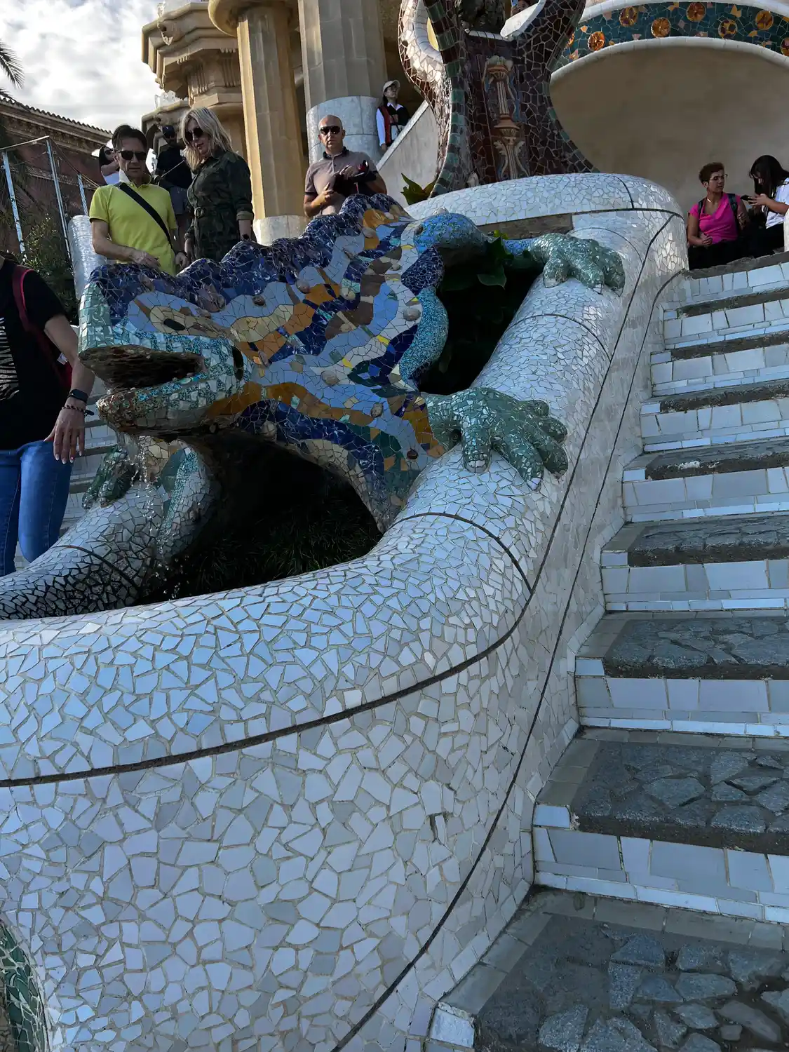 A long curved mosaic bench with visitors on the steps above it and trees behind.