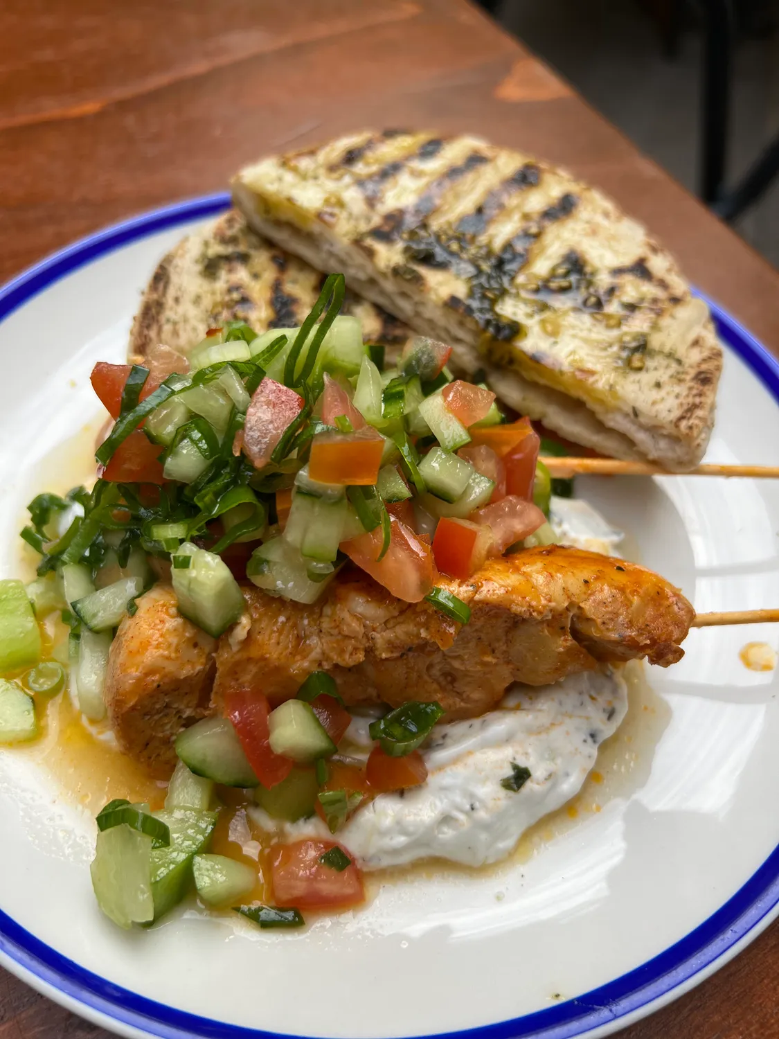 A plate of fried fish in a pale sauce with chopped salad, bread with a dark spread beside it.