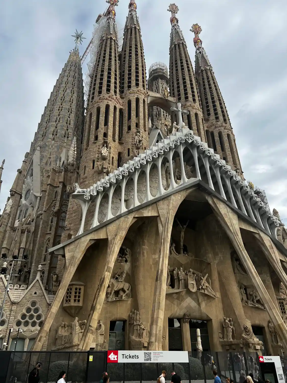 A great sculpted stone facade with towers and a crane above it, shops at street level under cloud.