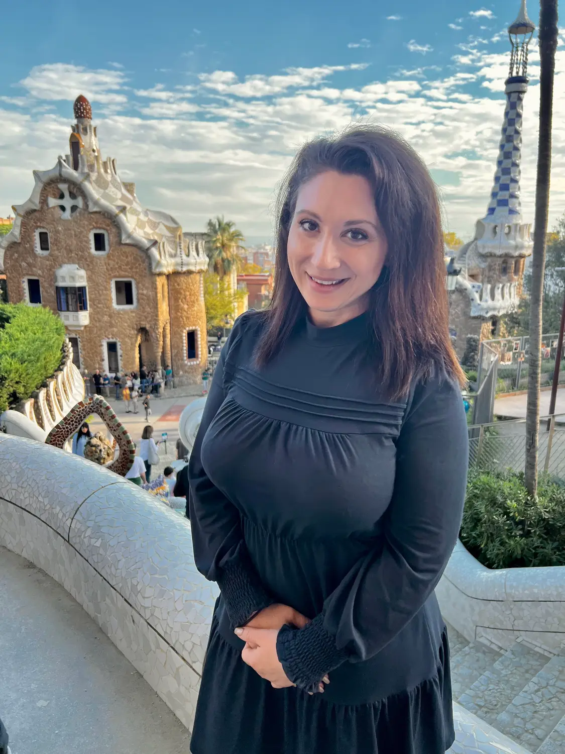 A woman in a dark dress on a terrace beside mosaic work, a mosaic tower behind her.