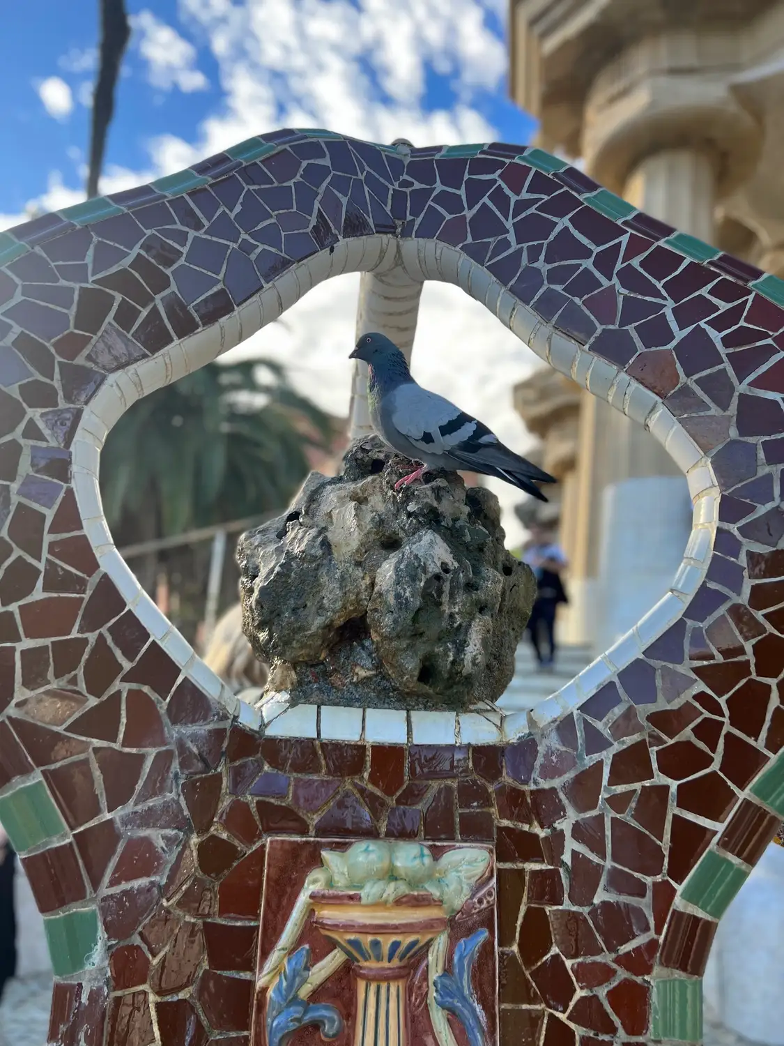 A pigeon perched in a tiled arched opening built of broken tile in many colours.