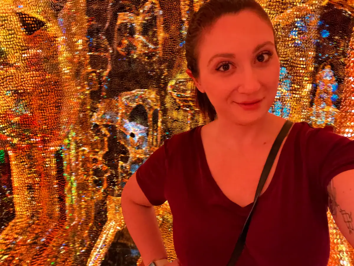 A selfie of a woman in a red top in front of an ornate mosaic wall of gold and blue.