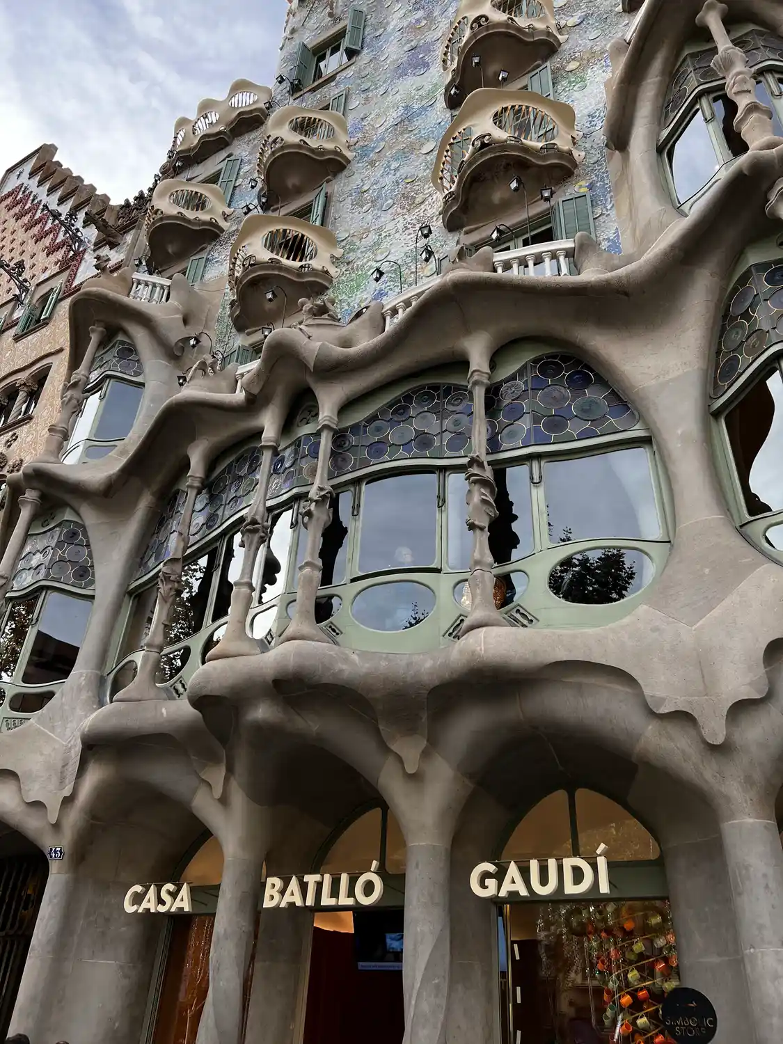 A sculpted stone facade carrying its own name in large letters, shops below it, seen from the street.