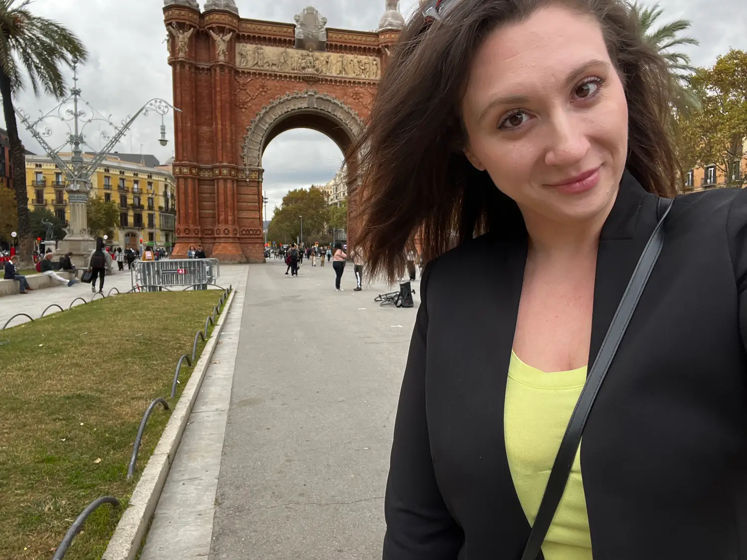 A selfie of a woman in front of a brick arch, a wide avenue stretching away behind her.