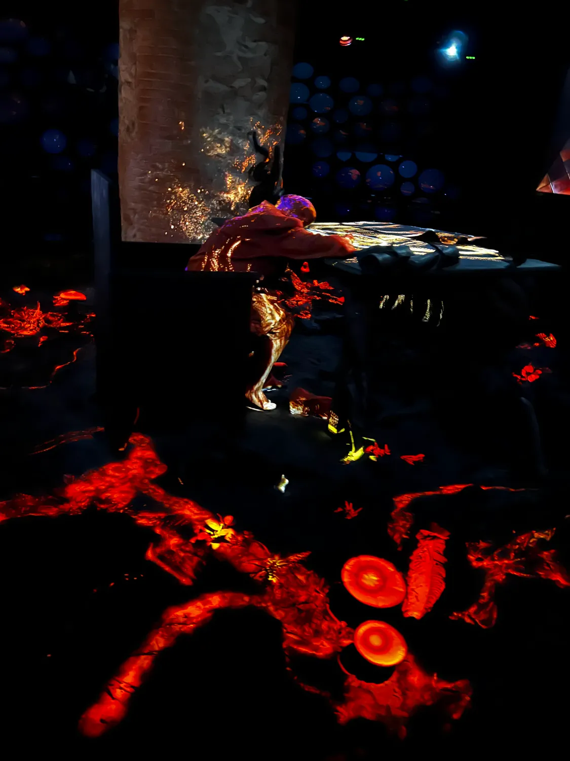 A dark room with forms lit red and orange glowing out of the black and a small lit trace low in the frame.