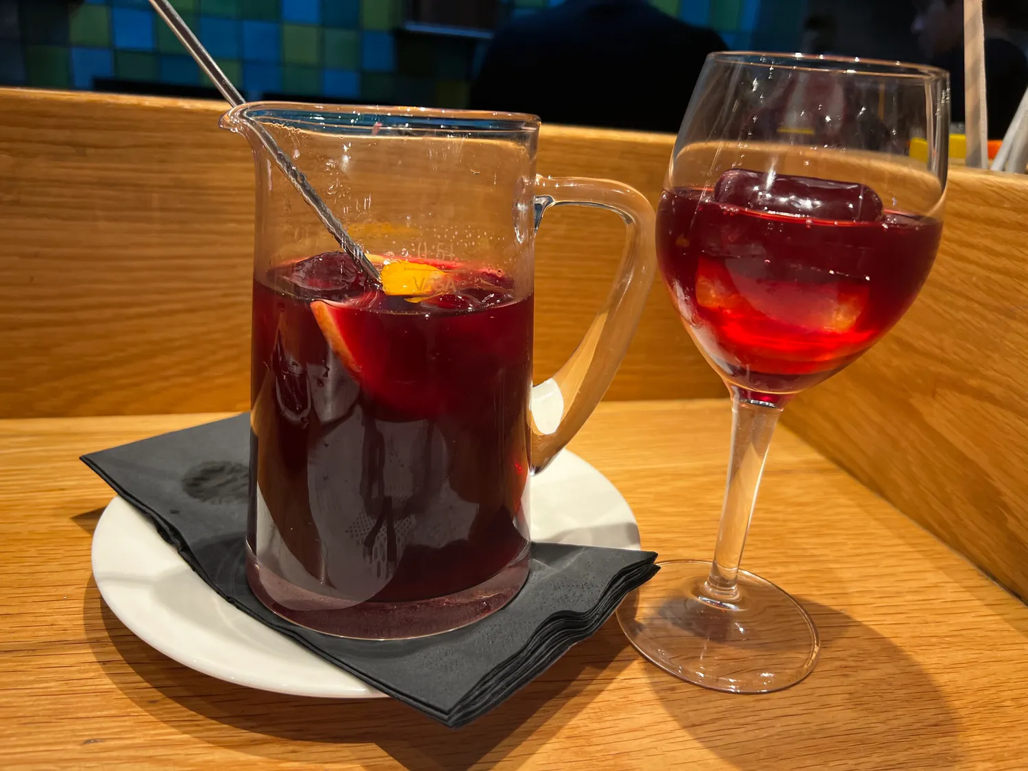 A glass mug of red wine with fruit in it and a glass of red wine beside it on a table.