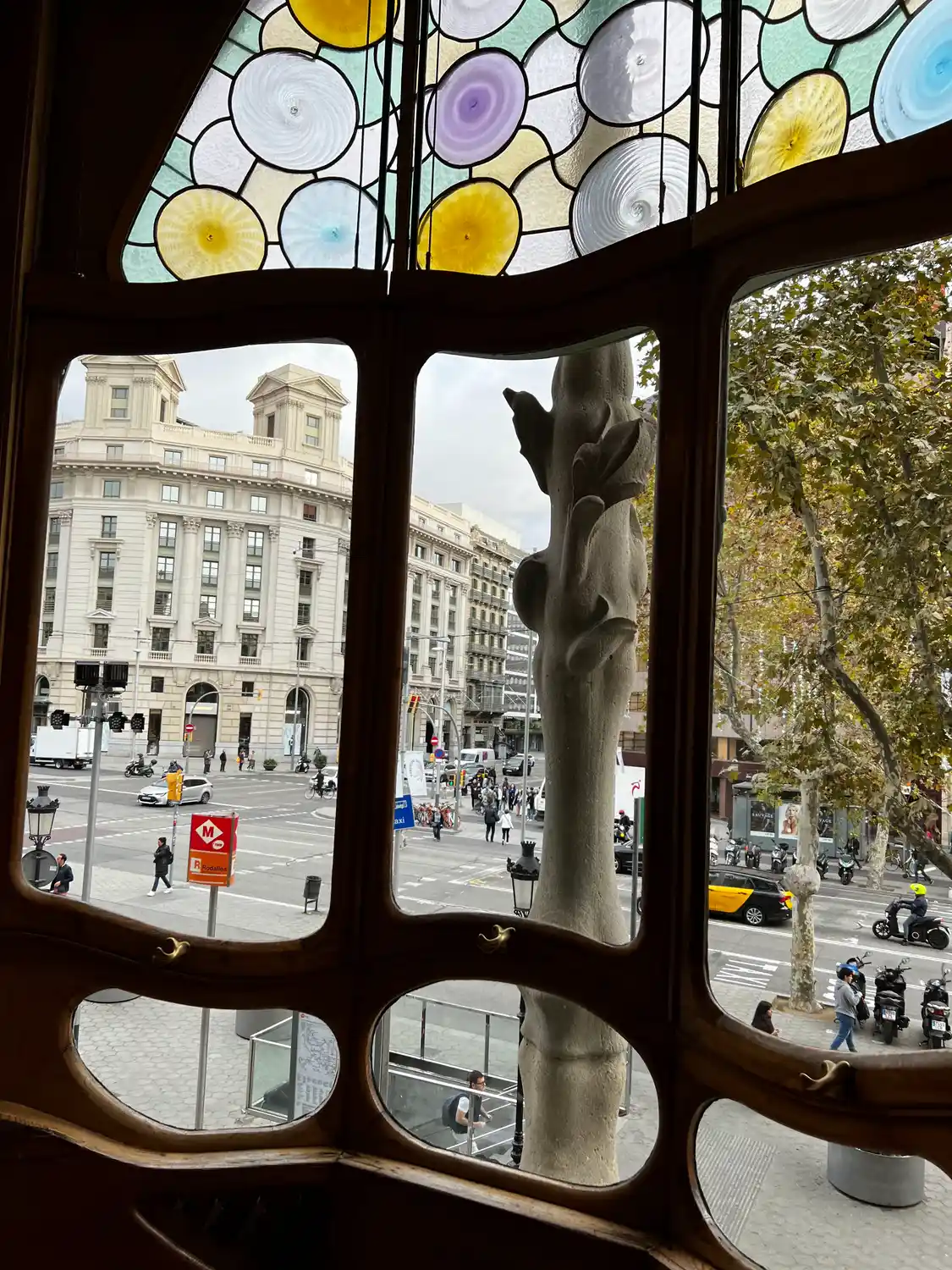 An ornate wooden window frame looking out over a plaza and a large building across it.
