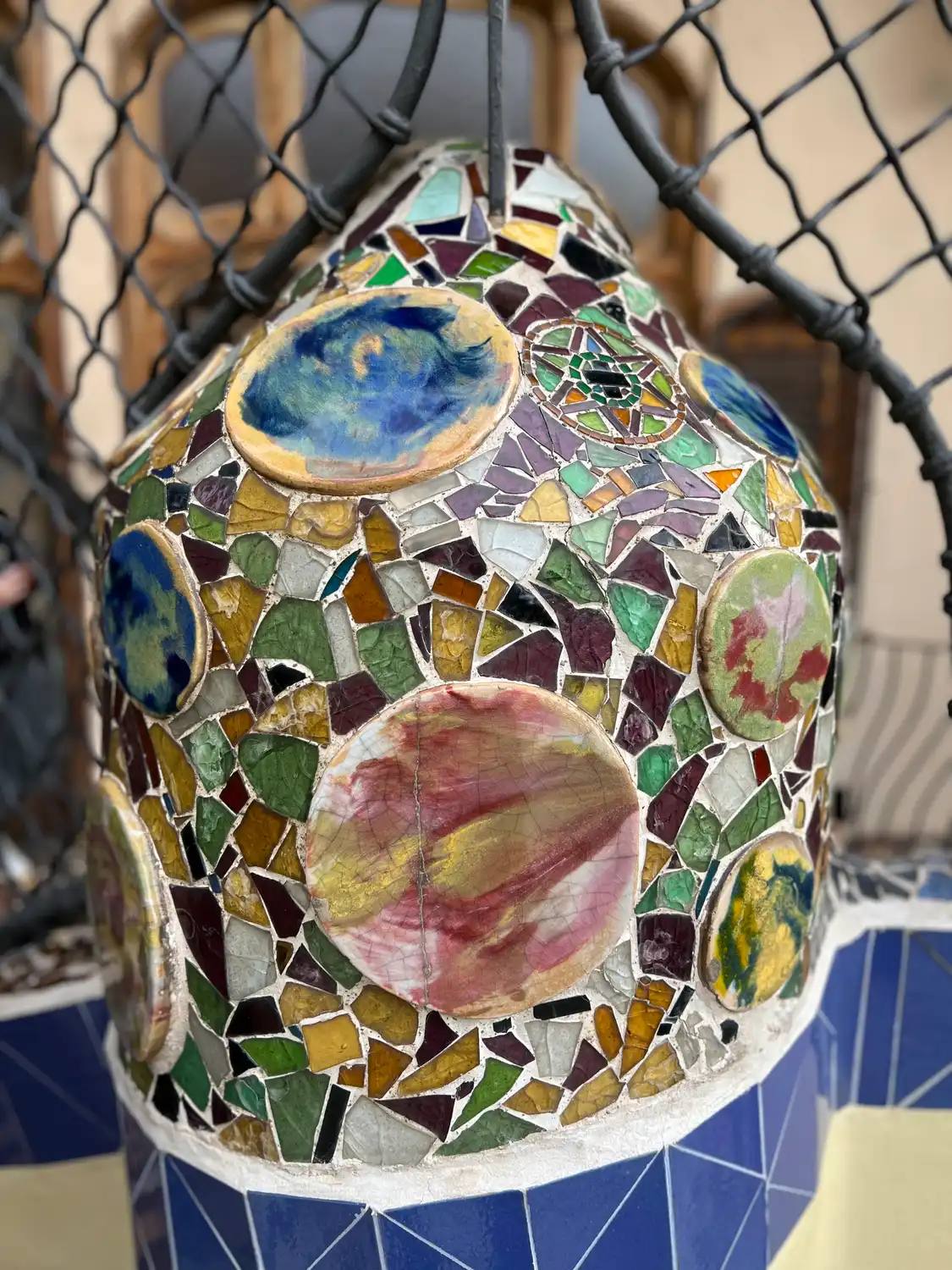 A large mosaic-covered form inside a rope net, with more mosaic discs stacked behind it.