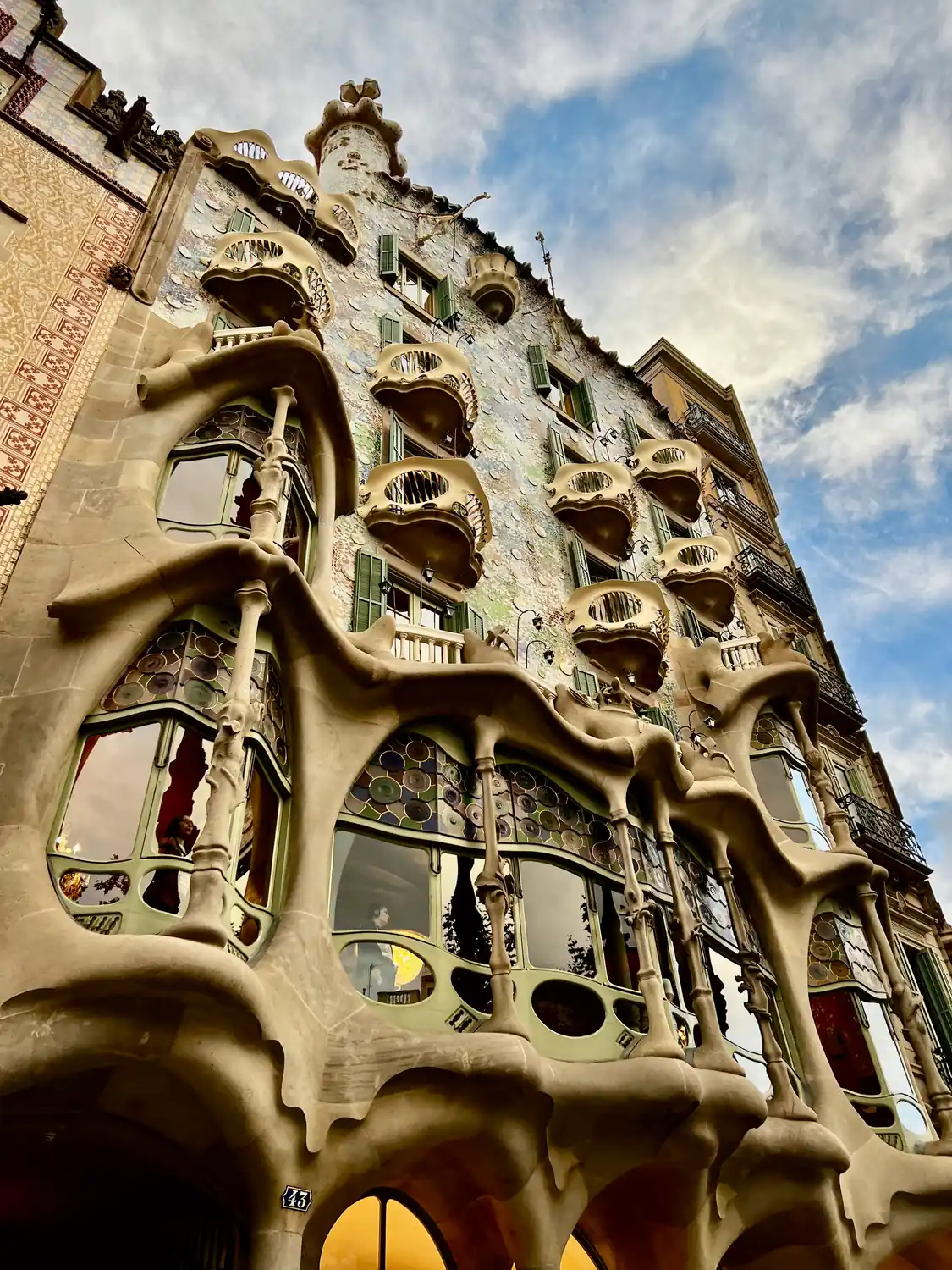 A tall carved stone facade with sculpted balconies and bone-like windows, seen from the street below against a blue sky.
