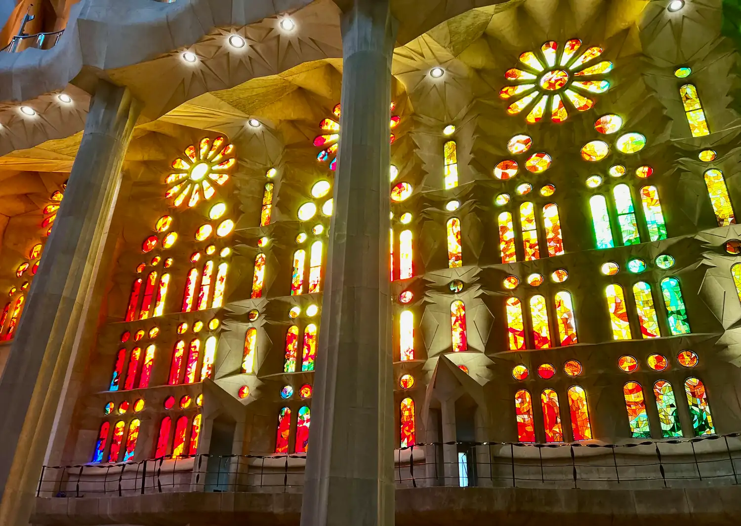 Tall columns standing between rows of stained glass in red, blue and gold inside a church.