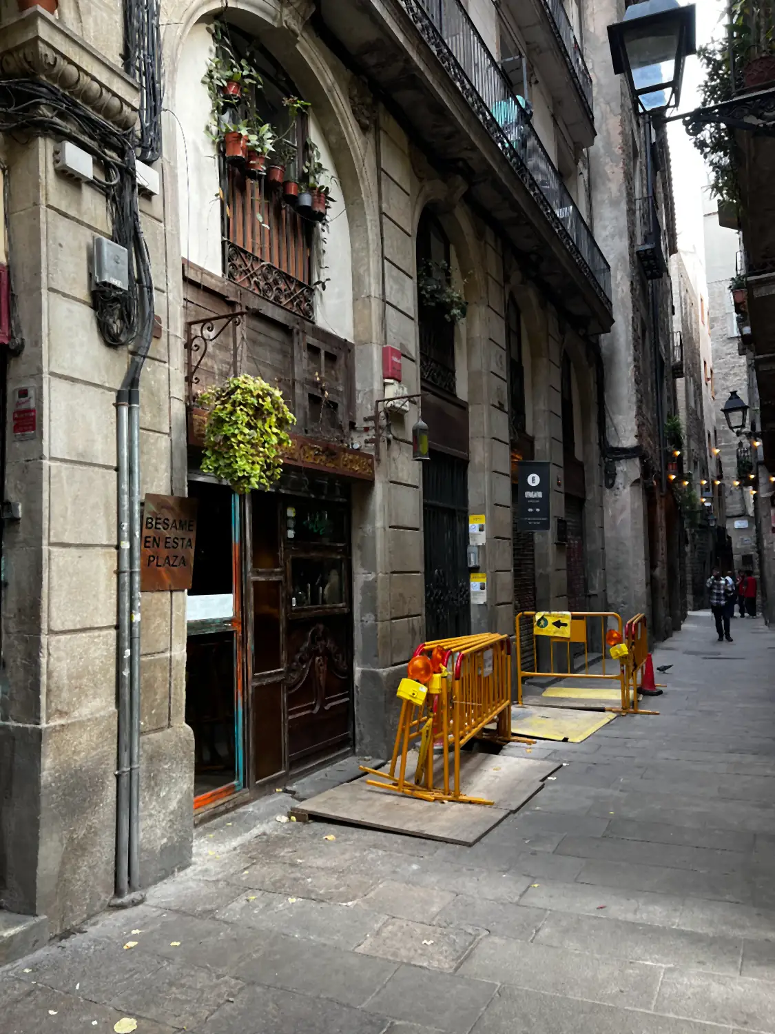 A stone lane with an old shop entrance, a hanging lantern, barriers and a one-way sign on the wall.