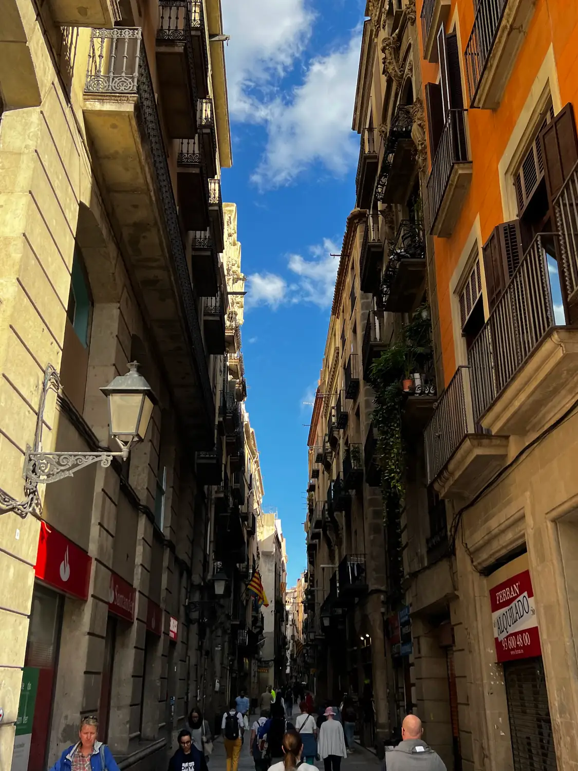 A narrow street running between tall buildings, with a red sign on the wall at the right.