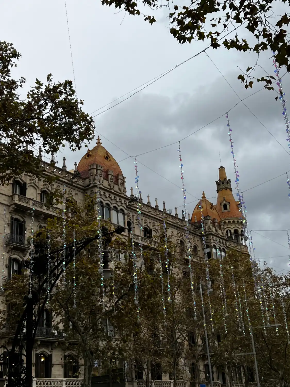 A heavy stone building with towers rising behind bare trees under a grey sky.