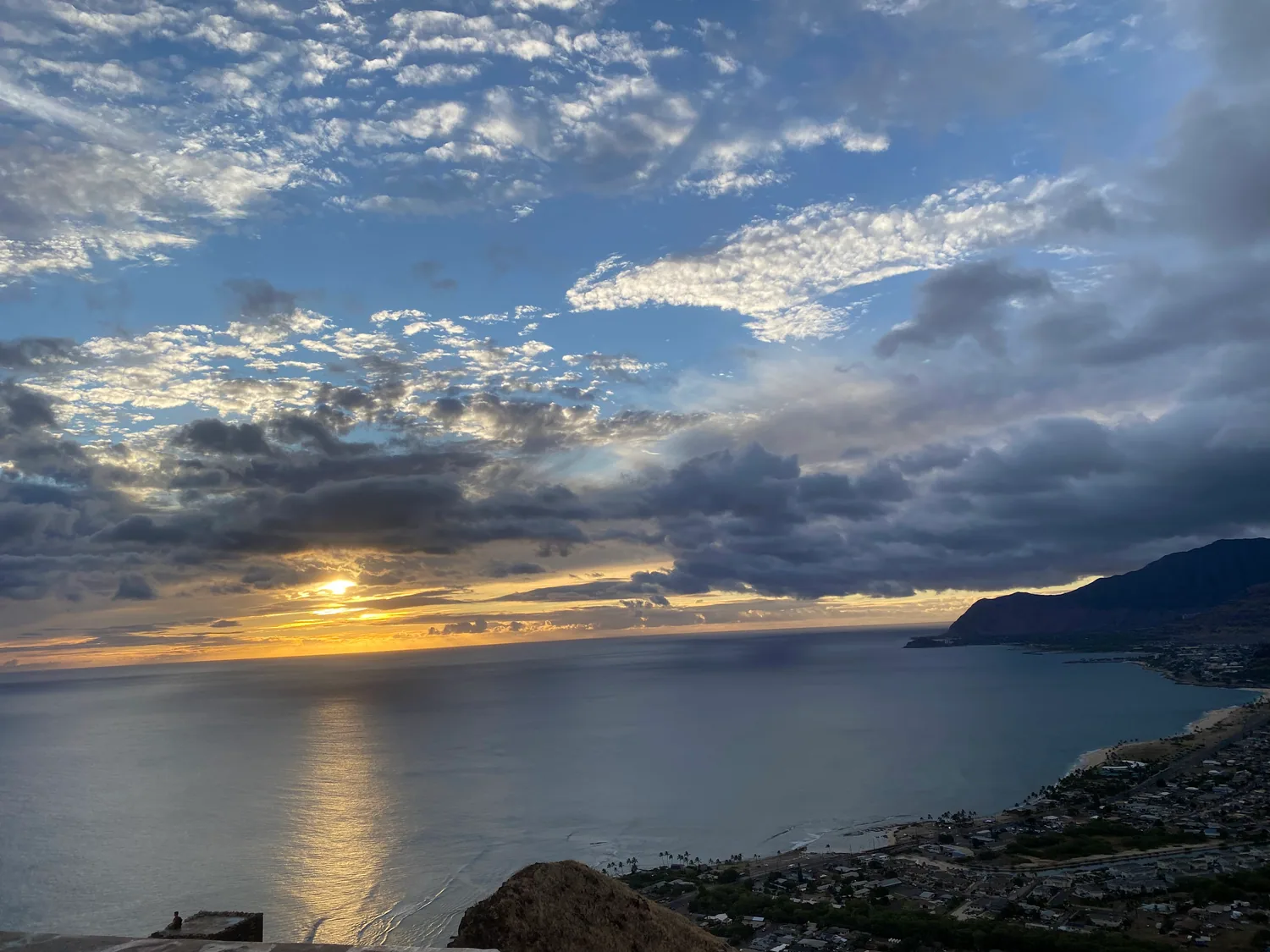 The sun setting over the sea behind cloud, with a headland and the coast below at the right.