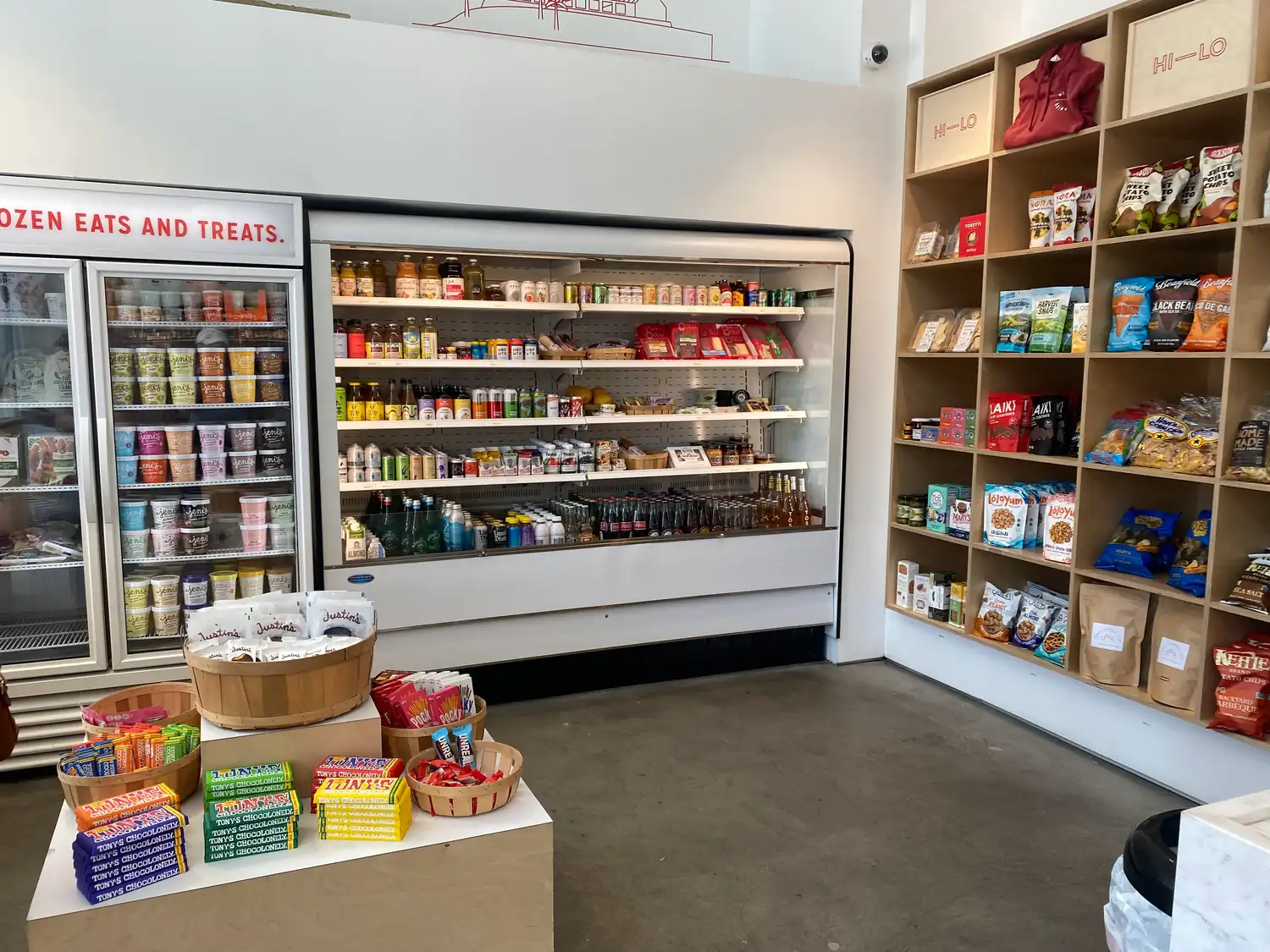 A shop aisle with glass-fronted fridges and shelves of packaged snacks.