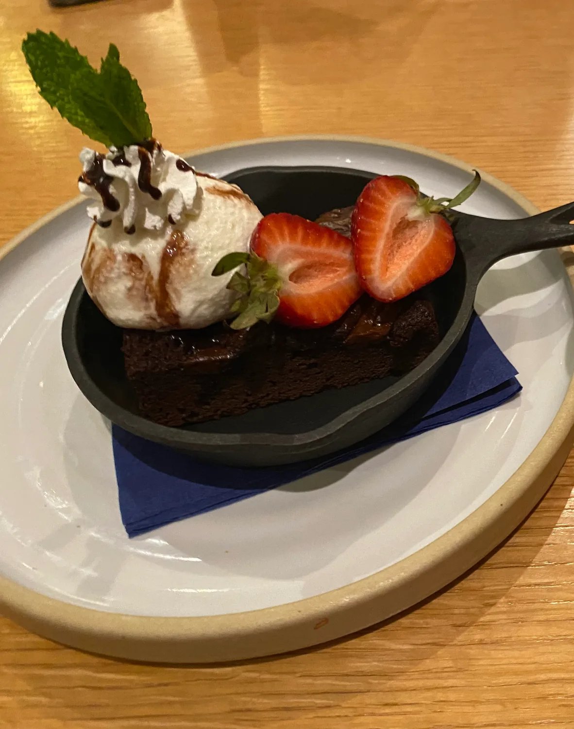A brownie with ice cream, strawberries and mint in a small pan on a wooden table.