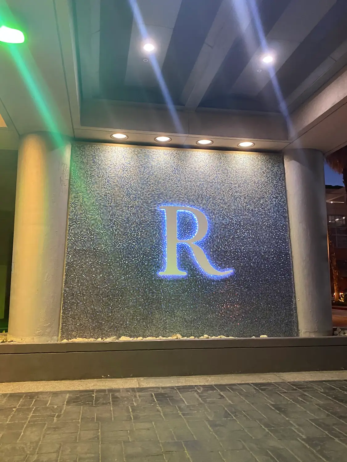 A tall stone lobby with a large glowing letter set into a mirrored wall, lit from above.