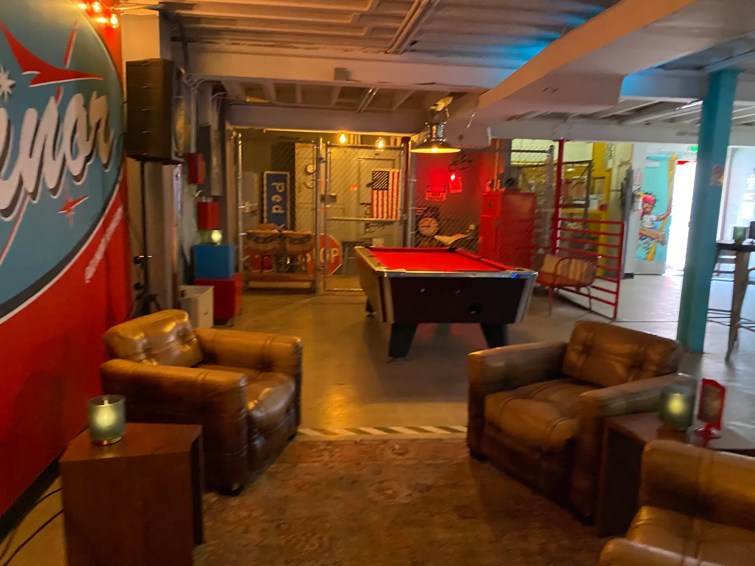 A lounge with leather armchairs, a pool table and a lit signboard on a red wall.