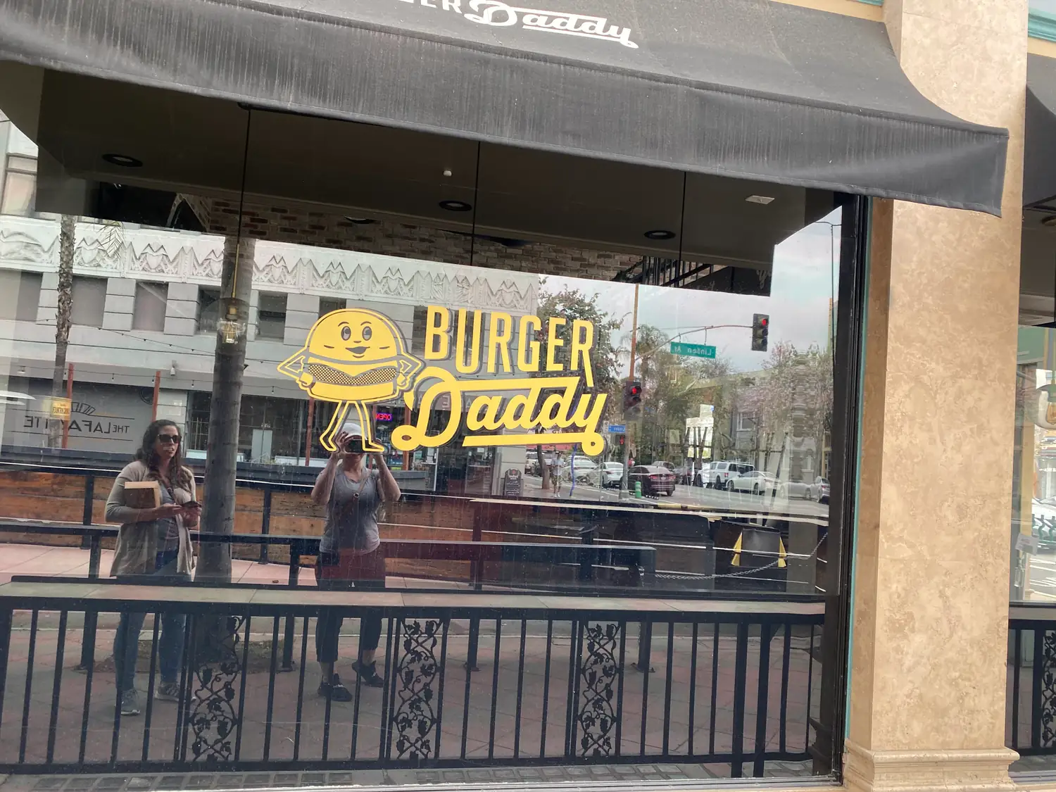 A street seen through a window from inside, painted lettering on the glass and people passing beyond a rail.