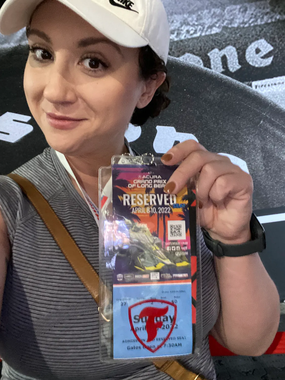 A woman in a cap holding up a laminated pass and a ticket, dark lettering on a wall behind her.