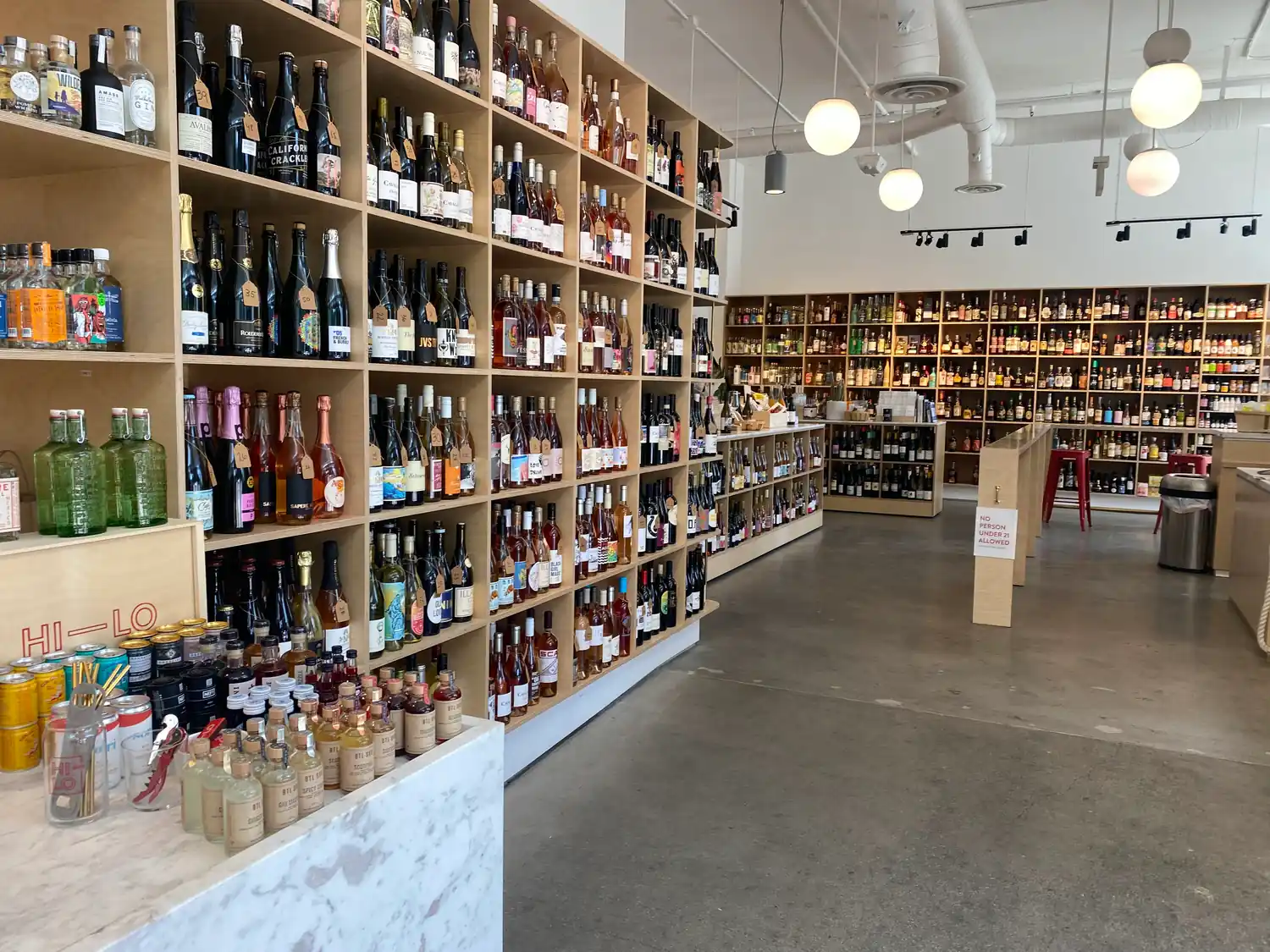 A wide shop floor with shelves of bottles running up the walls and lights hanging over the aisle.