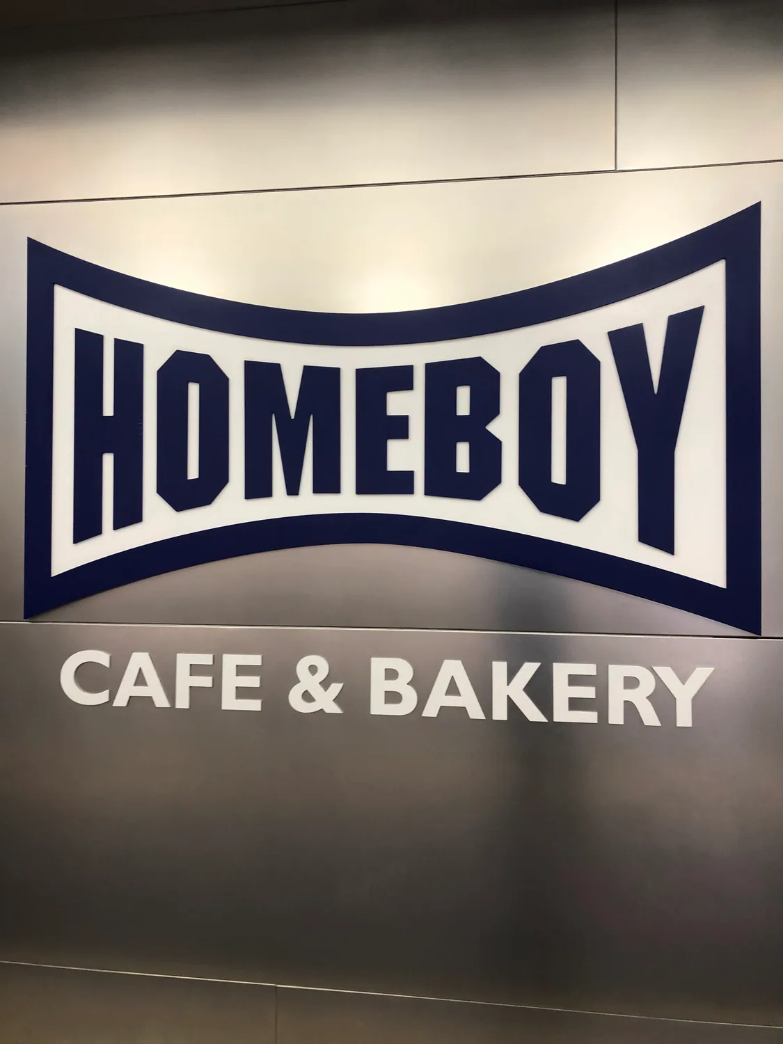 A large lettered sign with a curved border on a pale metal wall.