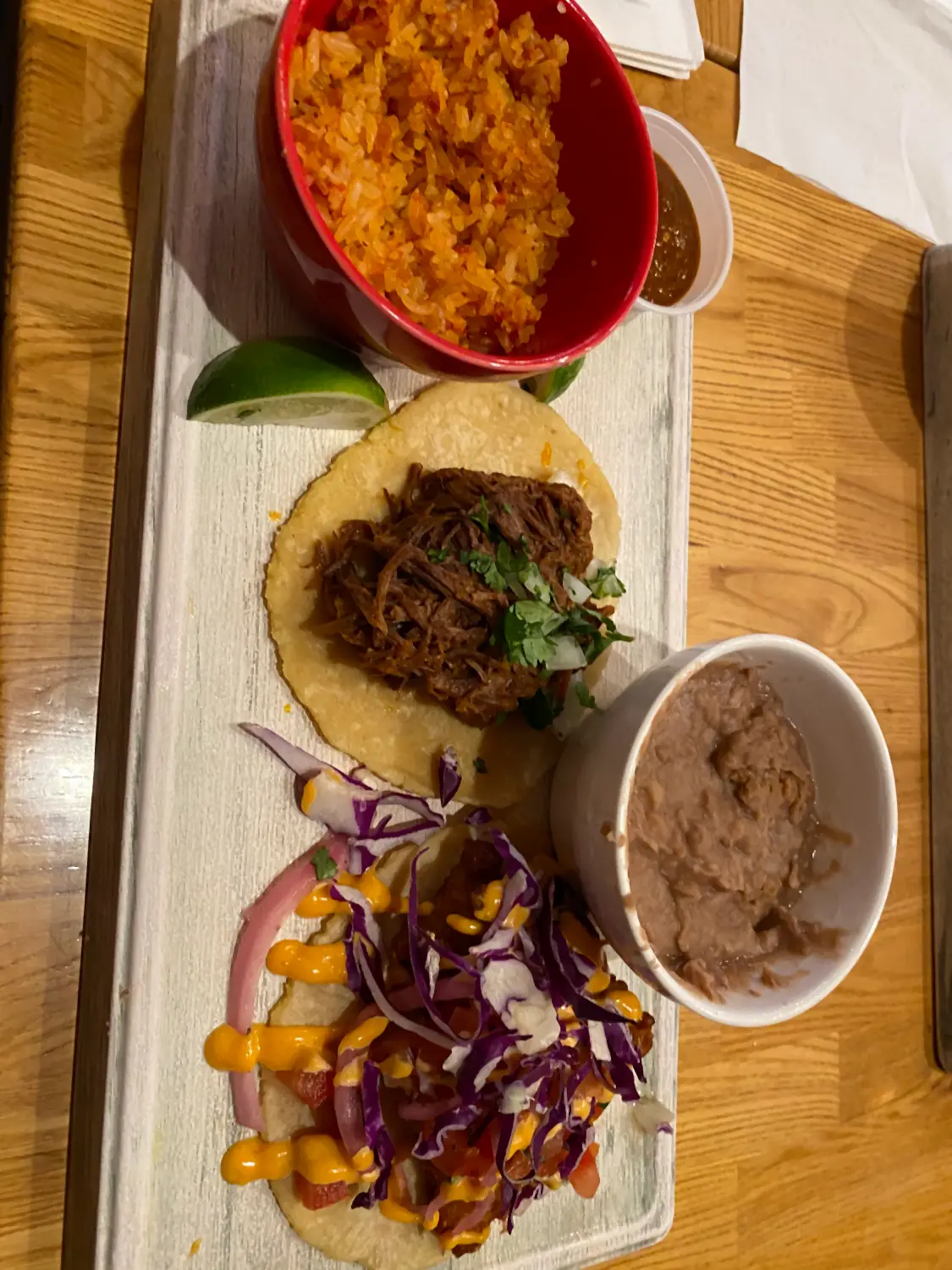 A tray of food seen from above: a filled bun, a plate of shredded cabbage and corn, and a small bowl.