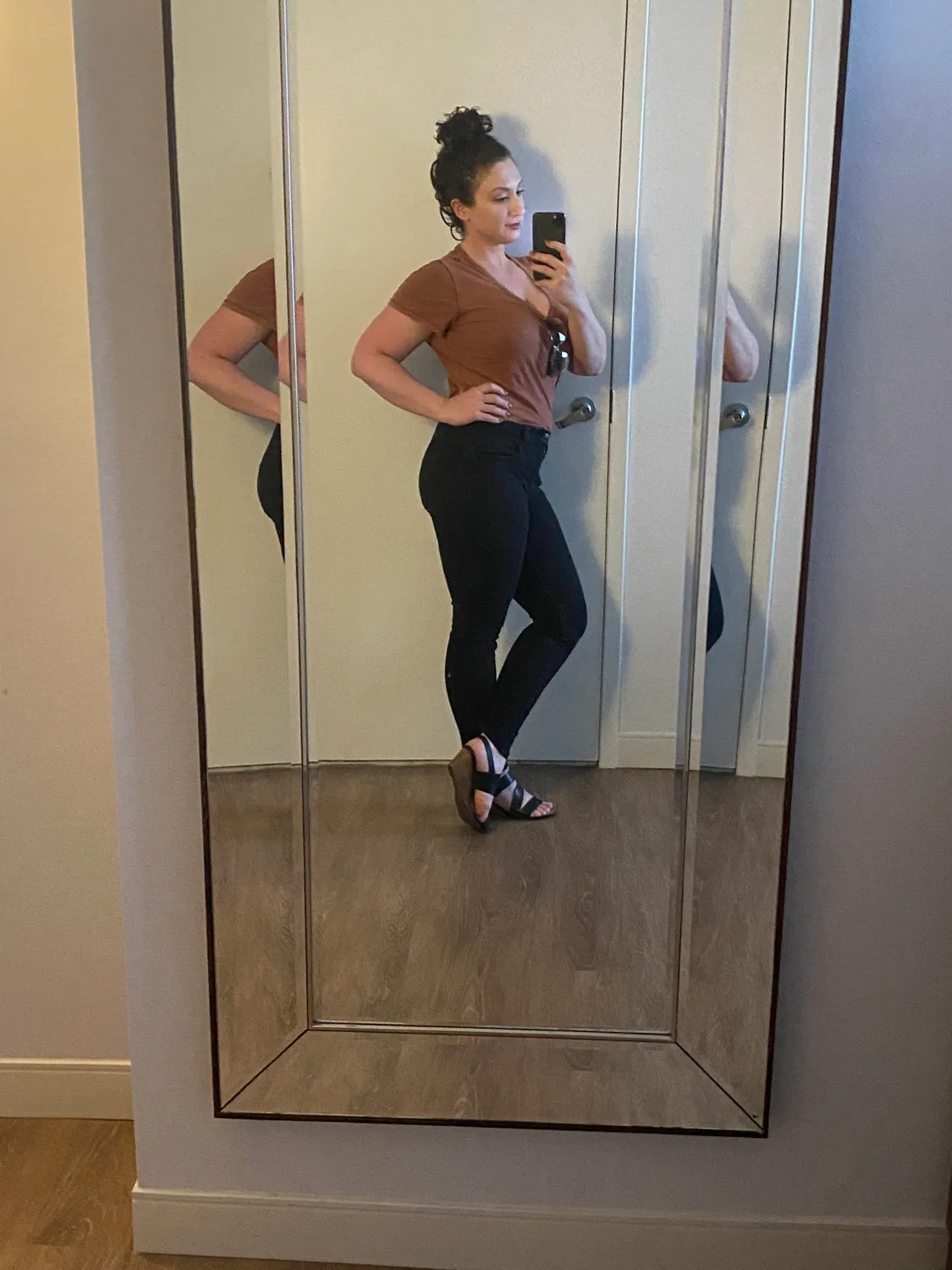 A woman in a dark top seen in a tall mirror, holding her phone up to take the picture.