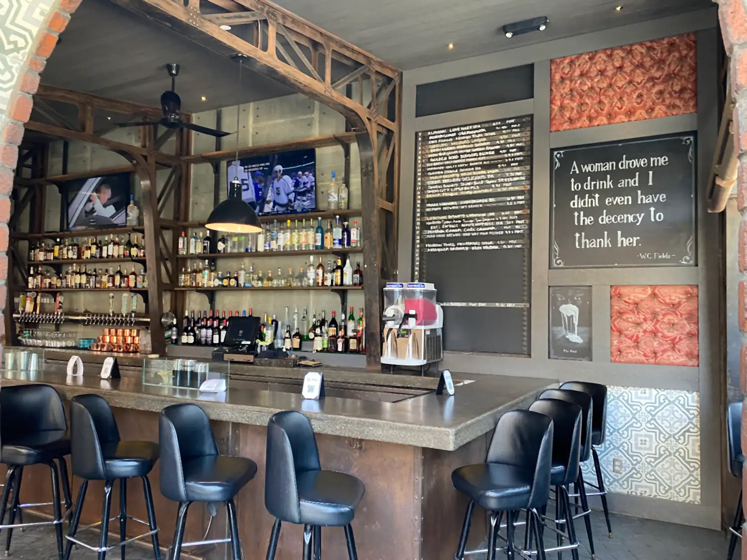 A bar counter with stools, shelves of bottles behind it and a wall of patterned tile.