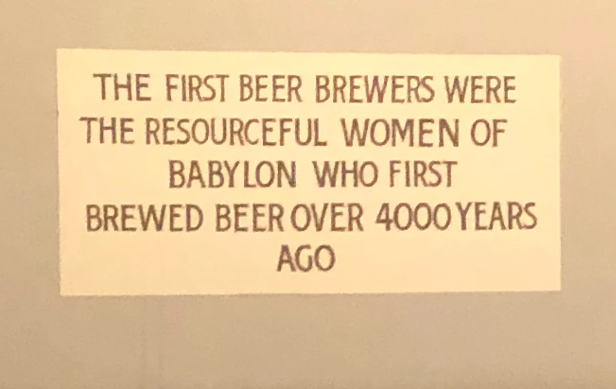 A small cream plaque on a plain grey wall, its lettering saying that the first beer brewers were the resourceful women of Babylon.