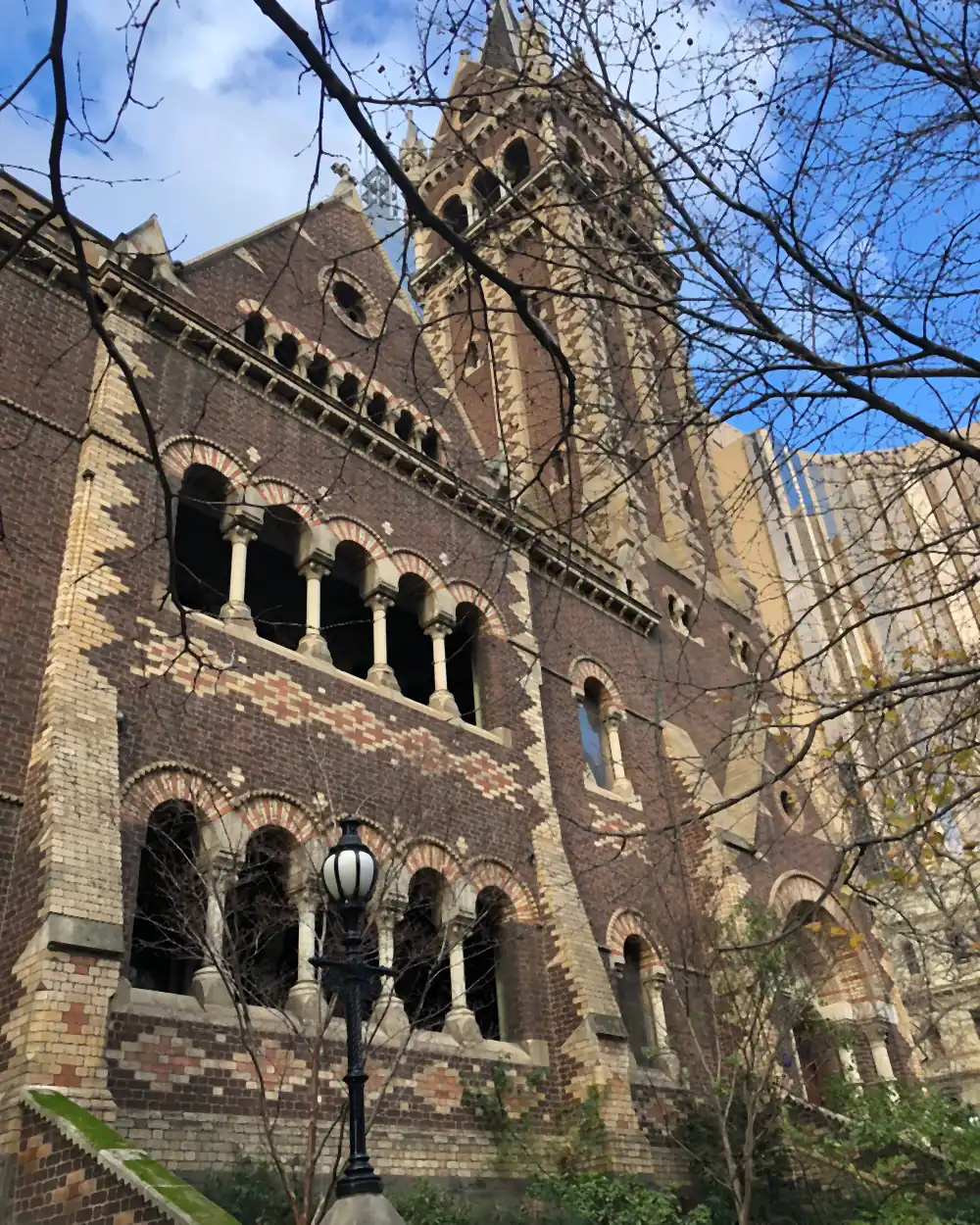 A brick and stone building with a tall tower and a row of arched windows, bare branches crossing the frame in front of it.