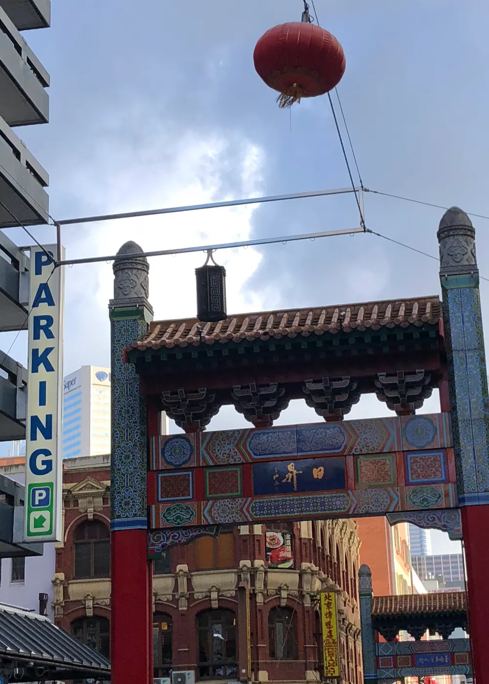 A gateway in red and blue with a tiled roof spanning a city street, a red lantern hanging above it.