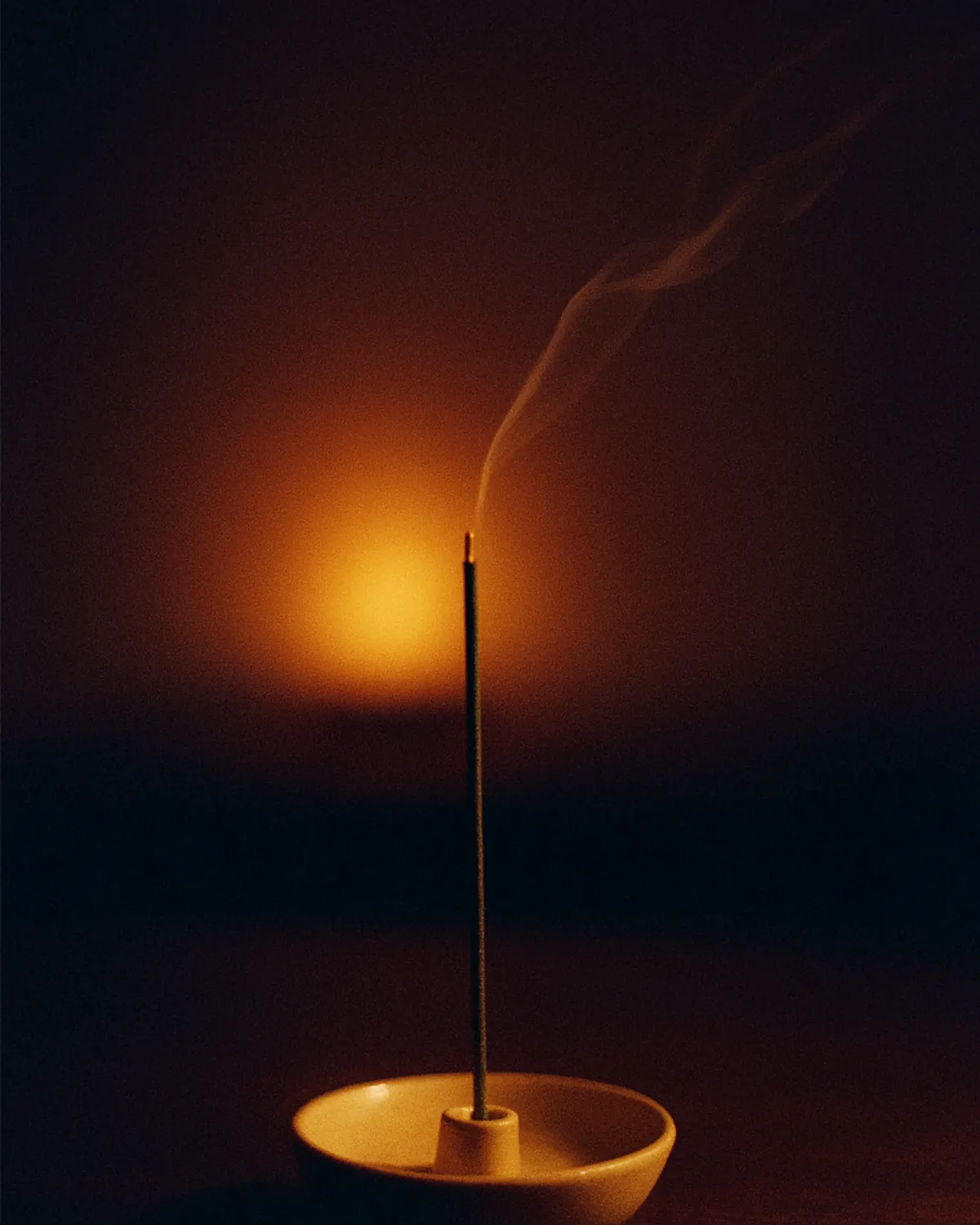 A stick of incense burning in a small holder at night, one thin line of smoke and a low light behind it. A generated placeholder image. Nothing has been made.