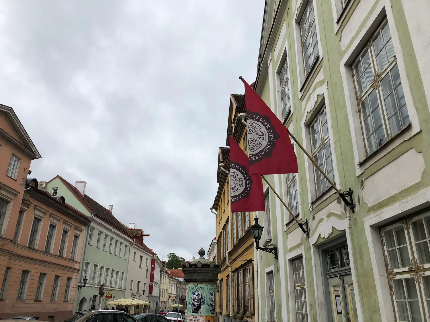 A street of old houses with two red flags carrying an emblem, hung from a facade.